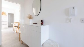 Ein stilvolles, minimalistisches Zimmer mit einem weißen Schrank, einem runden Spiegel, einer kleinen Vase mit Trockenblumen und einem weißen Stuhl.