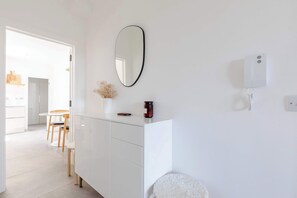Ein stilvolles, minimalistisches Zimmer mit einem weißen Schrank, einem runden Spiegel, einer kleinen Vase mit Trockenblumen und einem weißen Stuhl.