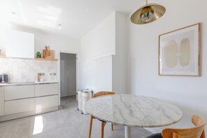 Uma cozinha moderna com armários brancos, bancada de mármore e um espaço de jantar com mesa redonda e cadeiras.