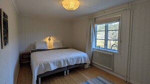 A bedroom with a bed, a nightstand, a window with curtains, a radiator, and a wall-mounted lamp.