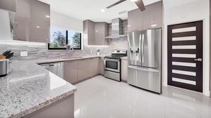 A modern kitchen with a granite countertop, stainless steel appliances, and a large window. - Villa Vivara, Luxury 7BR Retreat with Private Pool in Miami (North Miami Beach)