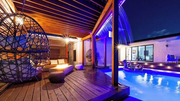 A wooden deck with a pool, a hanging chair, and a modern interior. - Villa Vivara, Luxury 7BR Retreat with Private Pool in Miami (North Miami Beach)