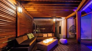 A wooden deck with a sofa, ottoman, and a table with a light. - Villa Vivara, Luxury 7BR Retreat with Private Pool in Miami (North Miami Beach)