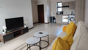 Un saló modern amb un televisor de pantalla plana, un sofà amb coixins grocs i una taula rodona petita.