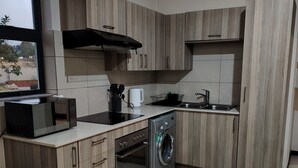 Una cuina compacta amb armaris de fusta, microones integrat, rentadora i una finestra amb vistes.