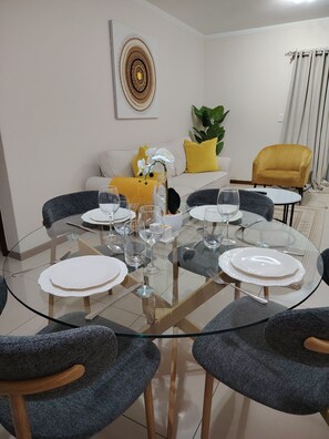 A dining area with a glass table, grey upholstered chairs, a white sofa with yellow cushions, and a yellow armchair. - Tranquil 2-Bedroom Apartment in Jackal Creek Golf Estate (Roodepoort)