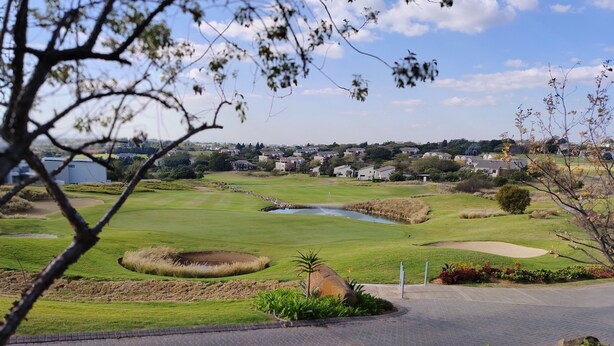 Ein Golfplatz mit Teich, Sandbunkern und Wohnhäusern im Hintergrund.
