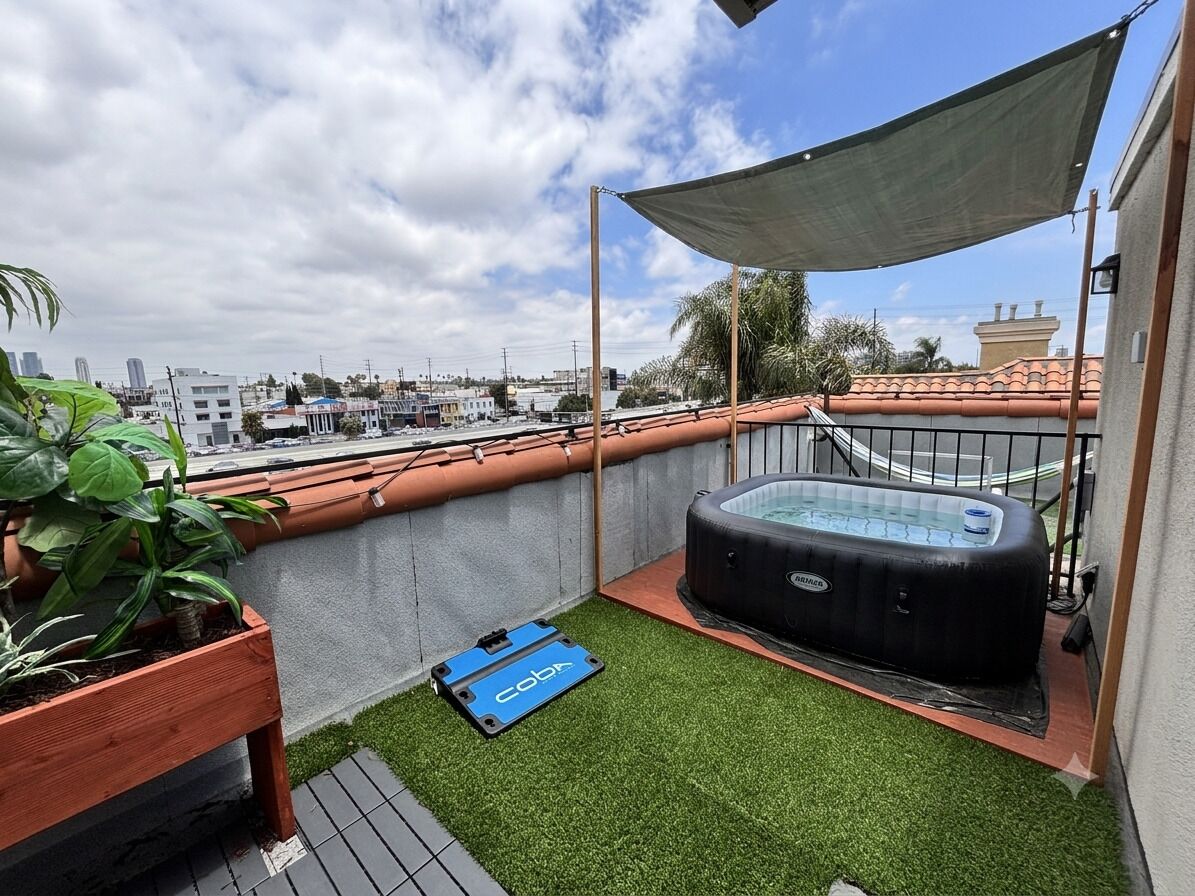 Eine Dachterrasse mit Whirlpool, Kunstgrasanlage, einem Holzpflanzgefäß und einem blauen Gegenstand am Boden.