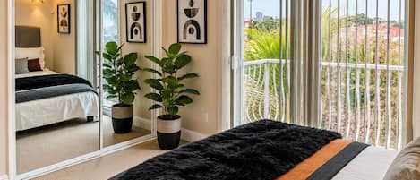 A bedroom with a bed, a large mirror, two potted plants, and a balcony with a railing.