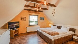 Ein Schlafzimmer mit einem Bett, einem Fernseher, einem Fenster und Holzbalken an der Decke.