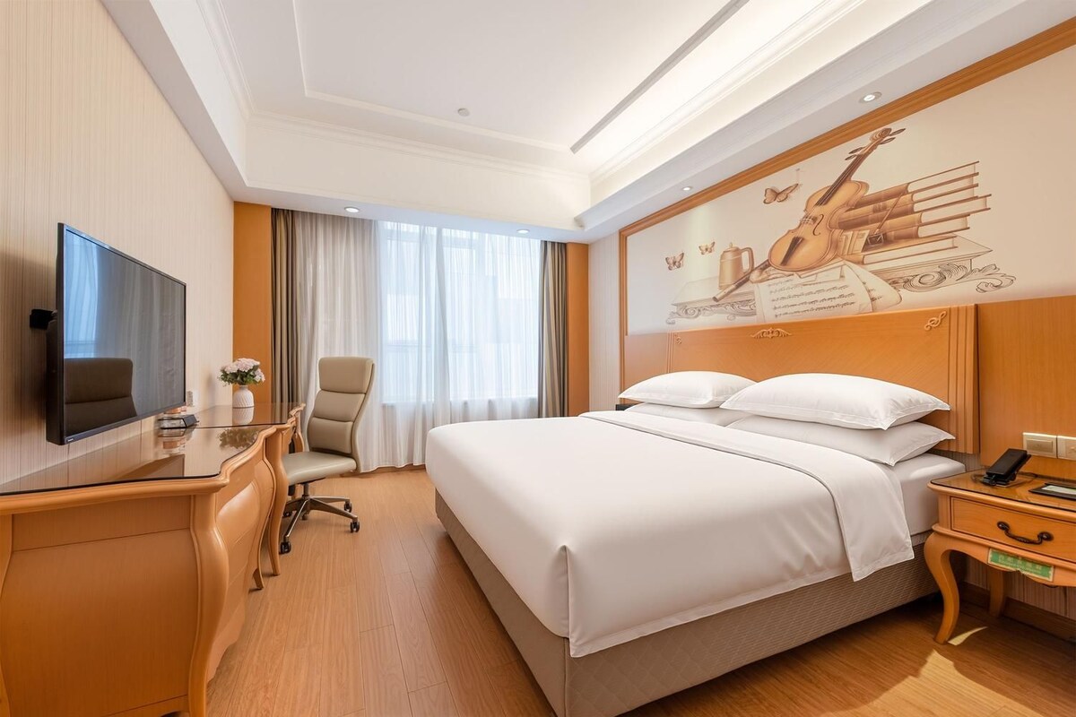 Ein Hotelzimmer mit Bett, Schreibtisch, Stuhl, Fernseher und einem Bild an der Wand.