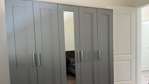 A grey wardrobe with mirrored doors and handles, a bed with a dark headboard, and a wooden floor.