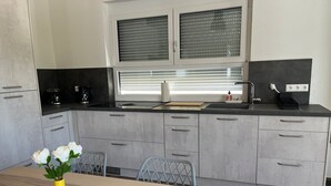 A modern kitchen with grey cabinets, a black countertop, and a window with blinds.