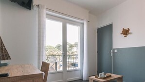 A room with a wooden table, a chair, a small table with cups, a television, and a door.