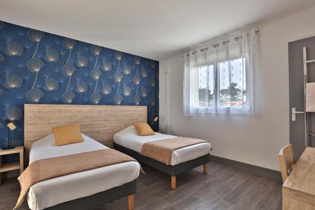 A hotel room with two beds, a large window with curtains, a wooden headboard, and a wall with a dandelion pattern.