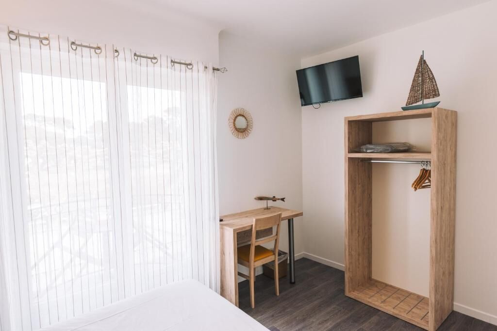A room with a bed, a desk, a chair, a TV mounted on the wall, and a wooden wardrobe.