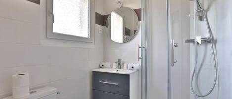Un baño moderno con inodoro, lavamanos, espejo y ducha.