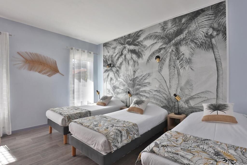 A room with two beds, a large wall mural of palm trees, a feather decoration, and a window with curtains.