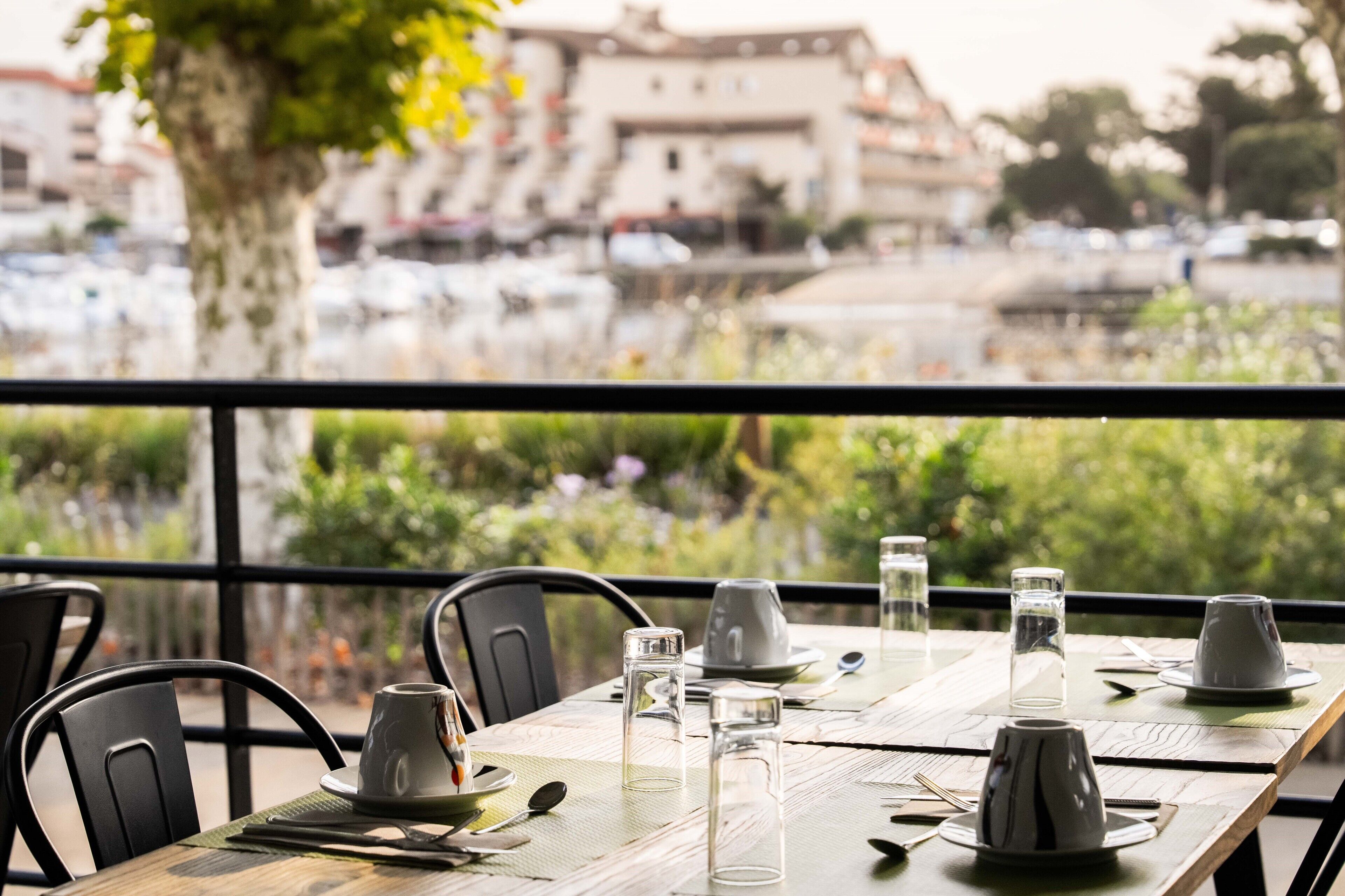 A table set for dining with chairs, a view of a marina with boats, and a building in the background.