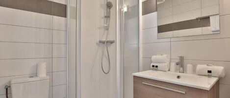 A modern bathroom with a glass-enclosed shower, a toilet, a sink with toiletries, and a mirror.