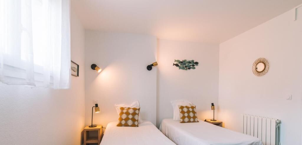A bedroom with two beds, bedside lamps, a radiator, and wall-mounted decor.