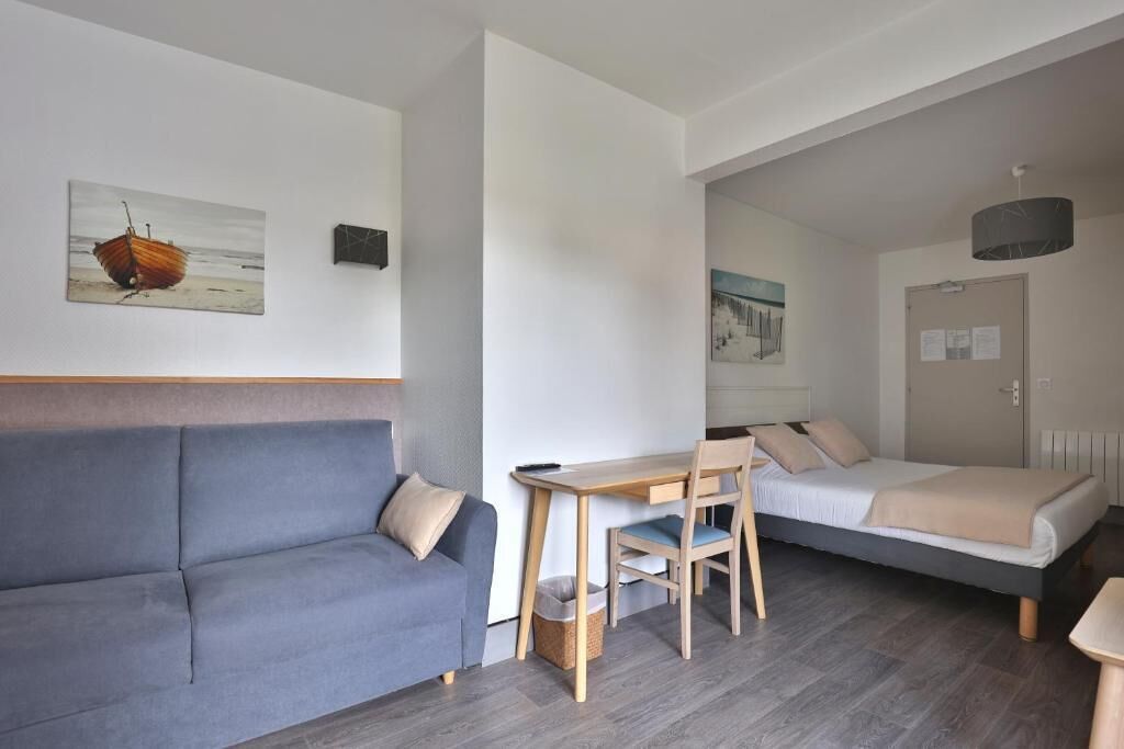Une pièce comprenant un canapé, un bureau avec une chaise, un lit et des œuvres d’art accrochées aux murs.