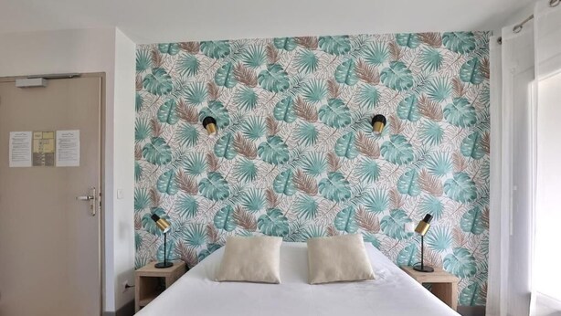 A hotel room with a large bed, two bedside tables with lamps, a door, and a wall with a tropical leaf pattern.