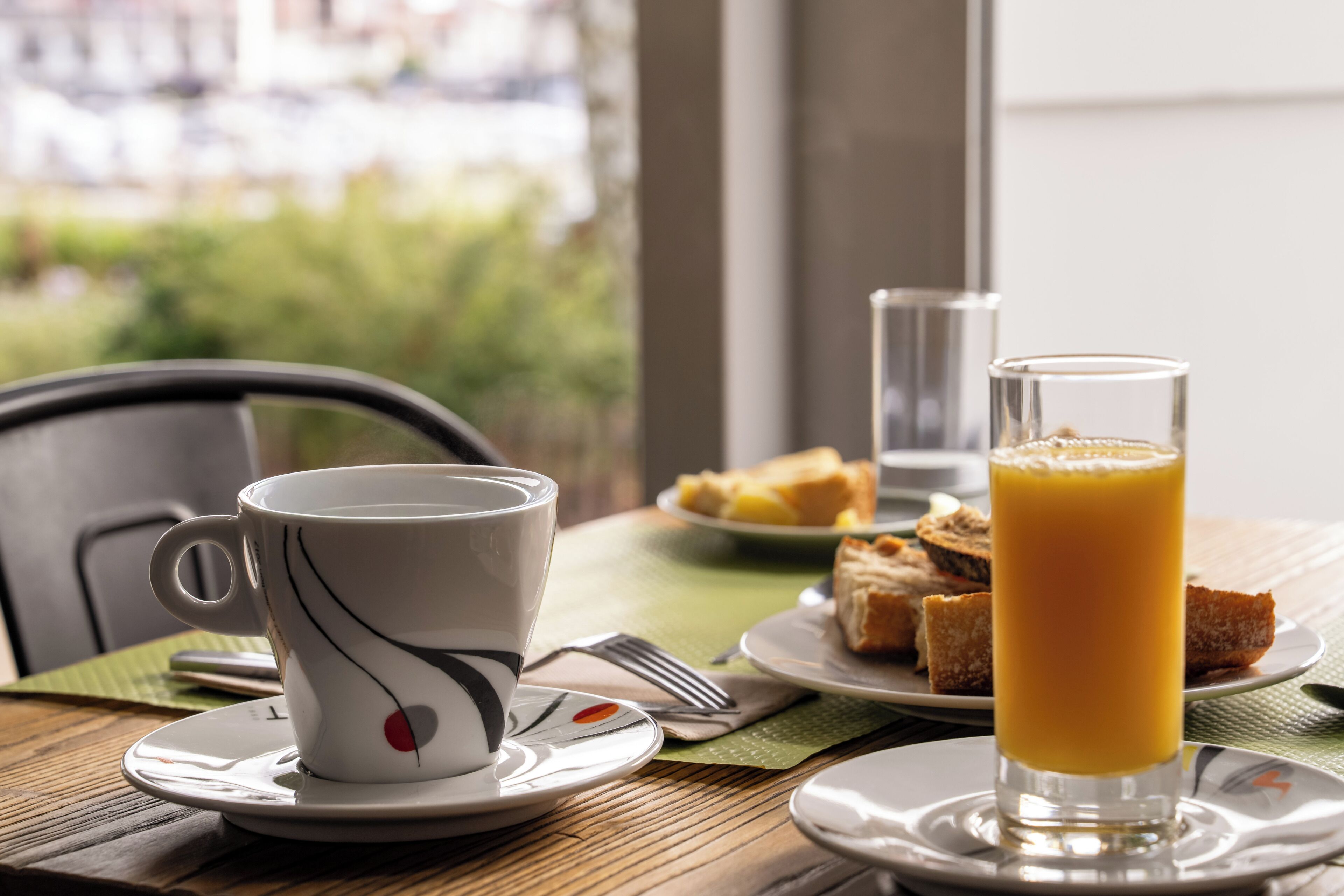Un desayuno servido con una taza, un vaso de jugo de naranja y una tostada sobre una mesa.