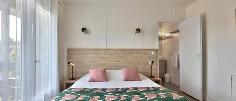 A bedroom with a bed, two bedside lamps, a headboard, and a wardrobe.