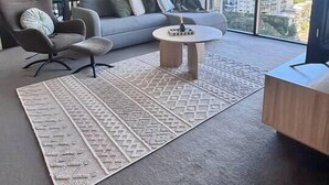 Un soggiorno moderno con divano, poltrona, tavolino da caffè e ampie finestre che offrono vista sulla città.