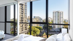Una camera d'hotel moderna con ampie finestre, un letto e vista sugli edifici circostanti.