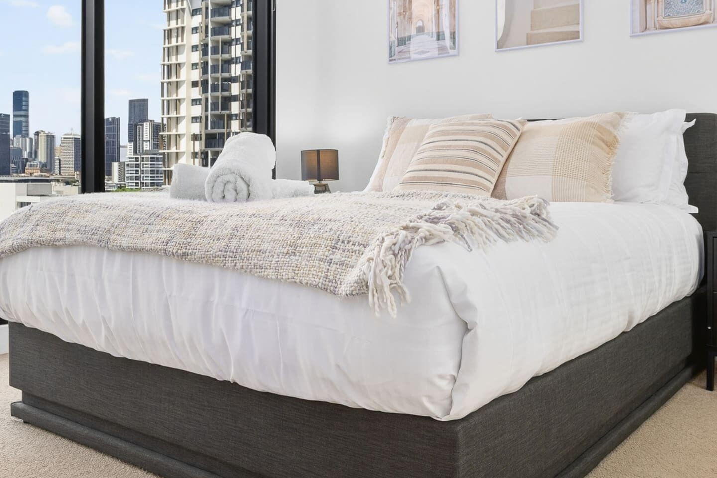 Een moderne slaapkamer met een groot bed en een stadszicht, met een stadsbeeld zichtbaar door het raam.