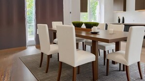A modern dining room with a wooden table, white chairs, and a view of greenery outside.