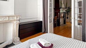 A bedroom with a bed, a fireplace, a desk, and a view into another room.