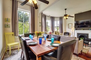 A dining area with a wooden table set for four, surrounded by chairs, with a television and fireplace in the background. - 1 Mi to SCAD! Historic Savannah Haven w/ Patio (Savannah)