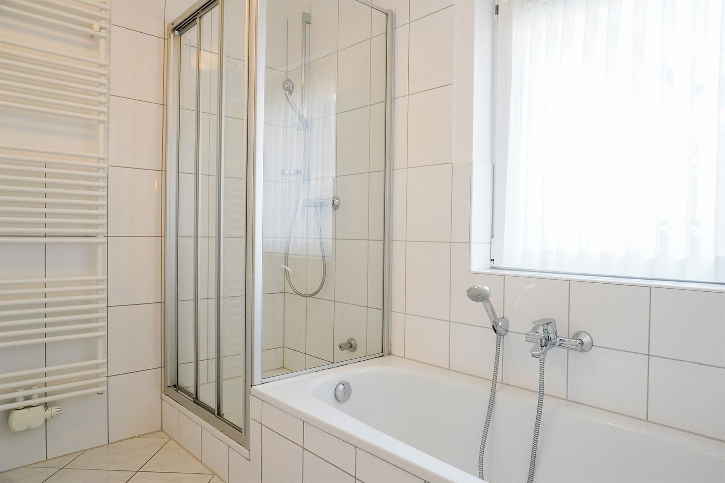 A bathroom with a glass-enclosed shower, a bathtub, and a window with blinds.
