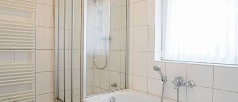 A bathroom with a glass-enclosed shower, a bathtub, and a window with blinds.