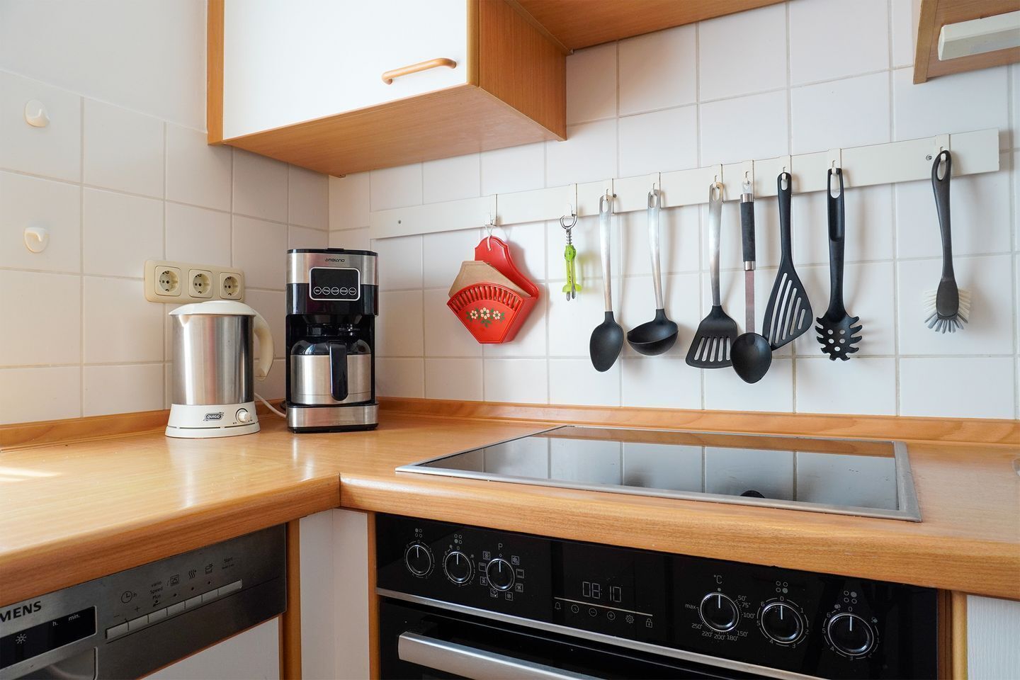 Eine Küche mit einer Kaffeemaschine, einem Wasserkocher, einem Herd und verschiedenen Küchenutensilien, die an der Wand hängen.