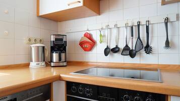 Eine Küche mit einer Kaffeemaschine, einem Wasserkocher, einem Herd und verschiedenen Küchenutensilien, die an der Wand hängen.