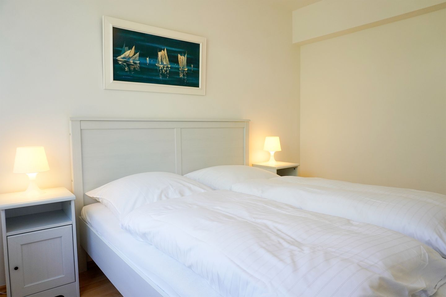 A hotel room with a double bed, two bedside tables with lamps, a nightstand, and a painting on the wall.