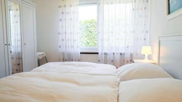 Ein Schlafzimmer mit Bett, Nachttisch, Lampe und einem Fenster mit Vorhängen.
