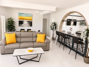 Ein modernes Wohnzimmer mit Sofa, Couchtisch und Essbereich mit Barhocker.