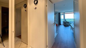 Ein Flur mit einer Tür, die auf einen Balkon mit Blick führt, einer Uhr an der Wand und einem roten Gegenstand auf dem Boden.