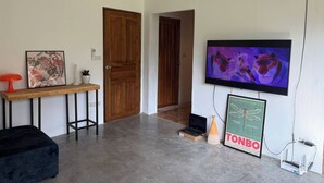 Ein modernes Wohnzimmer mit Holztür, einem an der Wand befestigten Fernseher, einem gerahmten Bild, einem kleinen Tisch und einem Laptop auf dem Boden.