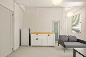 Ein kompakter Wohnraum mit einer Küchenzeile, einem Sofa und einem Fenster mit Jalousien.