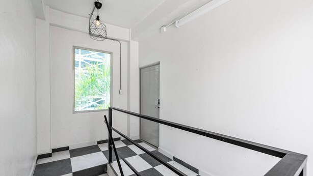 Uma escadaria com piso xadrez em preto e branco, corrimão de metal e uma janela com vista para o verde.