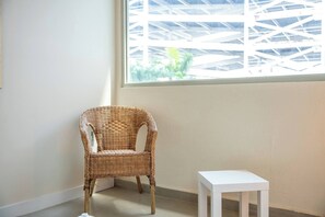 Ein Korbstuhl neben einem weißen Tisch in einem Zimmer mit einem großen Fenster.