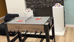 A ping pong table in a room with a stone fireplace, two white pillars with flowers, and a framed picture on the wall. - Chris          Manor (Saint-Augustin-de-Desmaures)