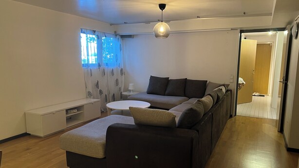 Ein stilvolles Wohnzimmer mit Ecksofa, rundem Couchtisch und Pendelleuchte.