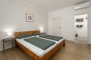 Una camera da letto con un letto di legno, due comodini con lampade, un quadro appeso alla parete e un bagno visibile attraverso una porta aperta.